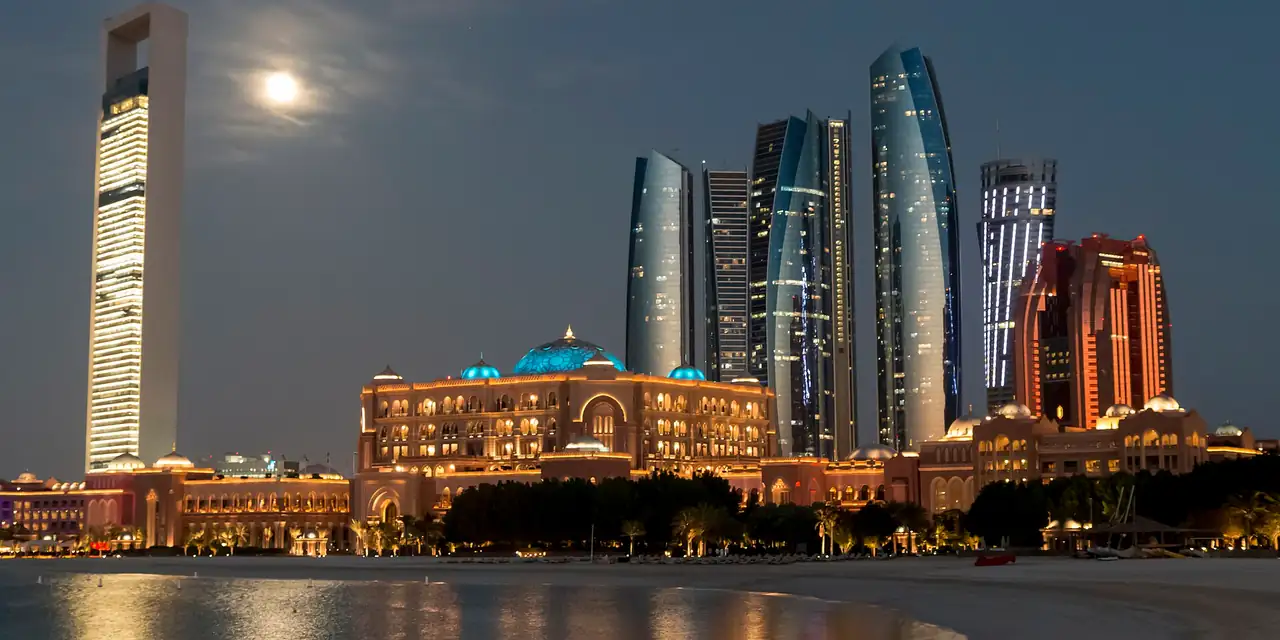 Etihad Towers and Emirates Palace in Abu Dhabi at night under a full moon